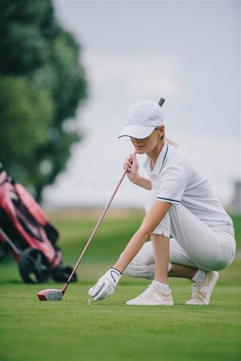 Female Golf Player In Cap And Golf Glove Putting Ball On Green Lawn