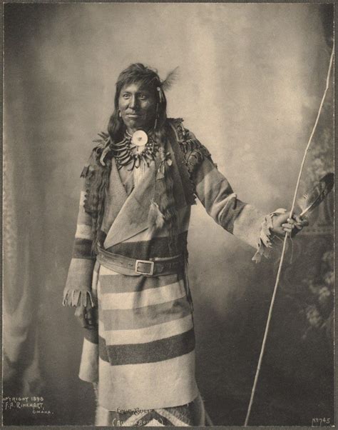 An Old Black And White Photo Of A Native American Man In Traditional Clothing Holding A Stick