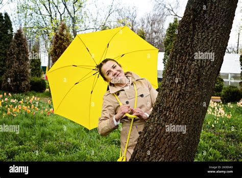 Happy Senior Woman In Yellow Rain Coat With Yellow Umbrella Walking In