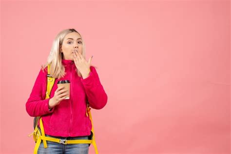 Vue de face femme blonde voyageur avec sac à dos mettant la main sur sa bouche tenant une tasse