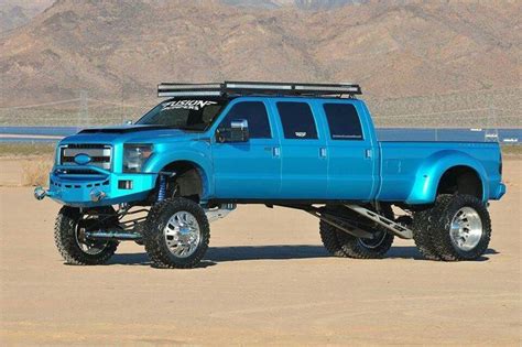 a large blue truck parked on top of a dirt field next to a body of water