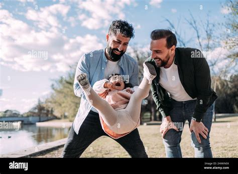 Alegre pareja gay jugando con su hija en el parque El padre hace pivotar a su niña en el aire