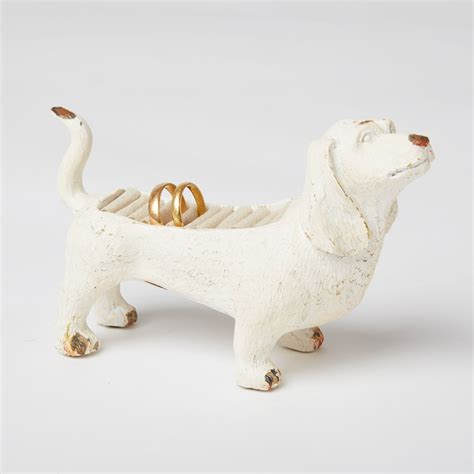 A White Dog Figurine With Two Gold Wedding Rings In Its Mouth