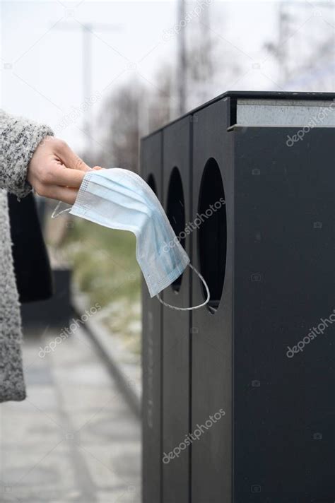 La mano femenina arroja la máscara médica usada al cubo de basura en la