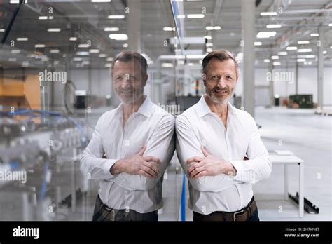 Mature Businessman Holding File While Leaning On Glass In Factory Stock