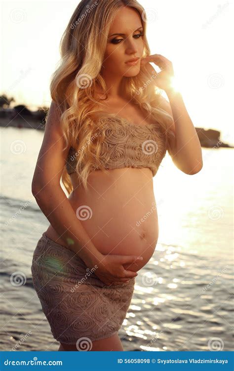 Mooie Zwangere Vrouw Met Het Lange Blonde Haar Stellen Op Zonsondergangstrand Stock Foto Image