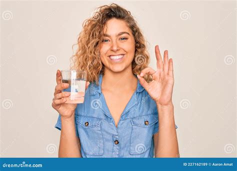 Jeune Belle Femme Blonde Aux Yeux Bleus Boire Un Verre D Eau Sur Fond Blanc Faire Ok Signe Avec
