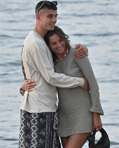 A Man And Woman Hugging On The Beach By The Water With Their Arms