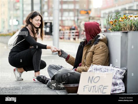 A Young Woman Giving Money To Homeless Beggar Man Sitting Outdoors In