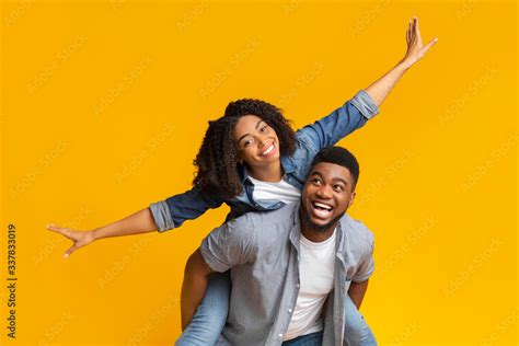 Cheerful African American Girl Riding On Boyfriends Back With Spreaded Hands Foto De Stock