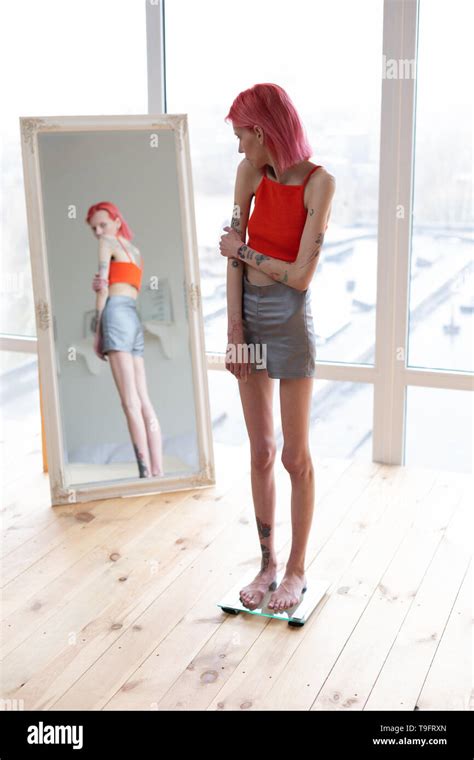 Anorexic Woman Standing On Scales And Looking Into Mirror Stock Photo