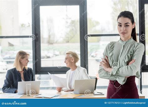 Attractive Young Businesswoman Standing With Crossed Arms At Meeting