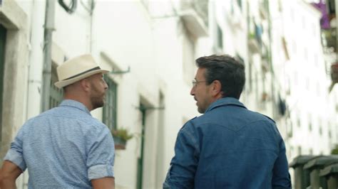 Vídeo Gratis Vista trasera de una pareja gay tomándose de la mano caminando por las calles de