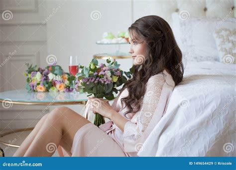 Sch Ner Junger Brunette In Einem Seidenhemd Sitzt Nahe Dem Bett Mit Einem Blumenstrau Von