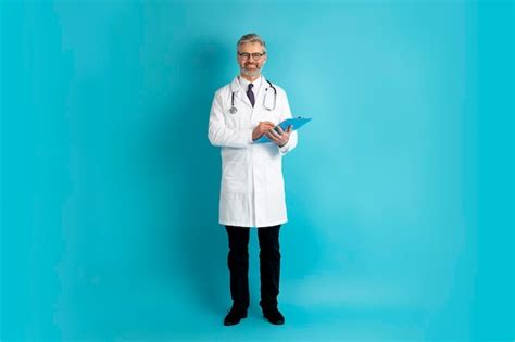 Médecin mature amical positif prenant l anamnèse sur fond bleu Photo Premium