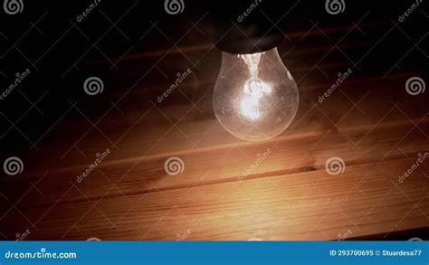 One Swinging Glowing Incandescent Light Bulb In Thick Smoke On Wooden