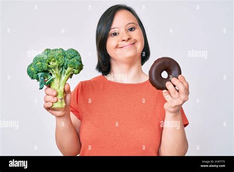 Brunette Woman With Down Syndrome Holding Broccoli And Chocolate Donut