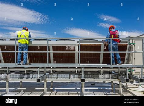 Two Construction Workers Work On An Adiabatic Condenser On The Roof At