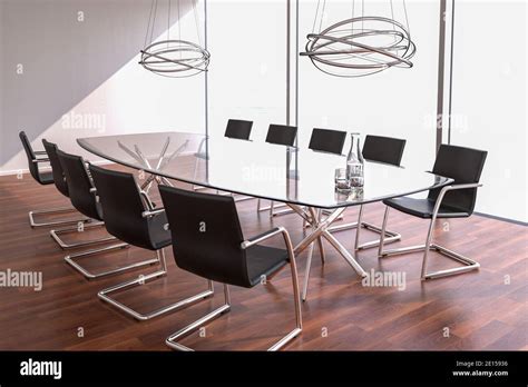 Brightly lit modern conference room with a large glass table, glasses and a carafe with water ...