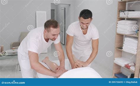 Two Male Massage Therapists Doing Massage Of The Legs Of A Young Girl