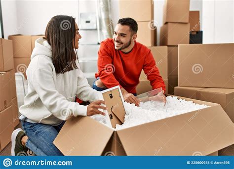 Young Latin Couple Smiling Happy Unboxing Cardboard Box At New Home