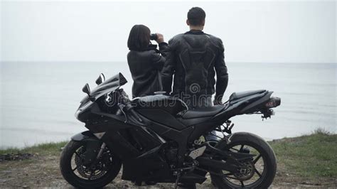 Back View Of Couple Of Young Bikers Standing On River Bank And Looking