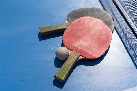 Two Table Tennis Or Ping Pong Rackets And Ball On Blue Table With Net