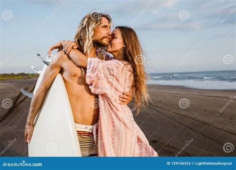 Handsome Surfer Hugging Attractive Girlfriend And Holding Surfboard On