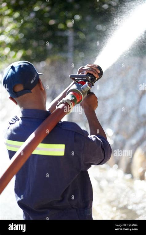 Fireman At Work Rearview Shot Of A Fireman Spraying Water With A Fire