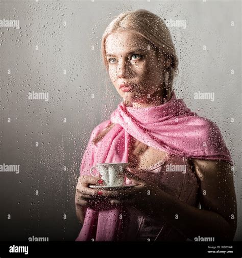 Young Blonde Woman Behind Glass With Water Drops Beautiful Girl Drinks