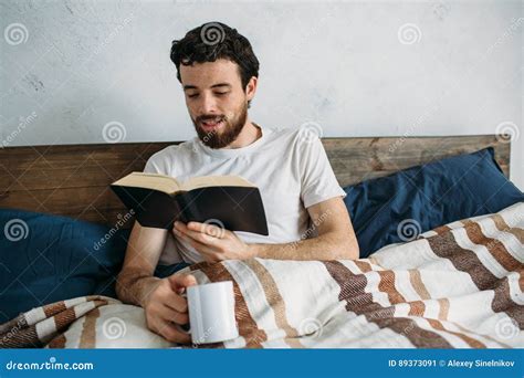 Bearded Man Reading A Big Book Lying In His Bedroom Stock Image