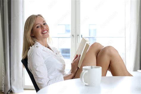 Hübsche blonde Frau mit nackten Beinen sitzt an einem Tisch hält ein Buch in den Händen und