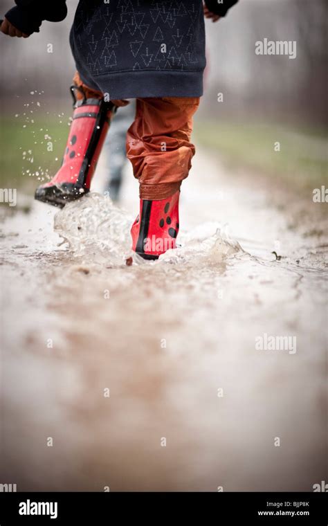 Young Boy Wearing Rain Boots Walks Through A Puddle Of Water Stock