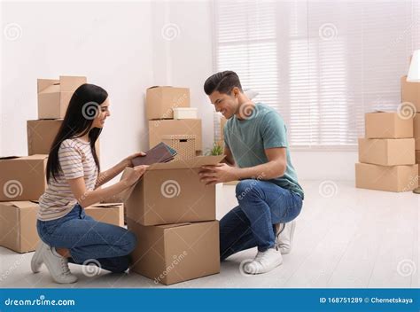 Happy Couple Unpacking Cardboard Boxes In Their Flat On Moving Day