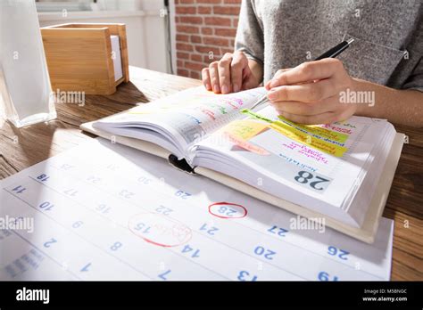 Close Up Of A Businesswoman Marking Schedule On Calendar From Diary At