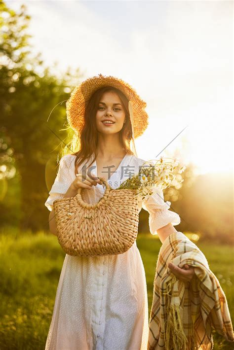 夕阳从背后照亮的田野中一位微笑的女人的肖像，她手里拿着一篮花和一条毯子高清摄影大图 千库网