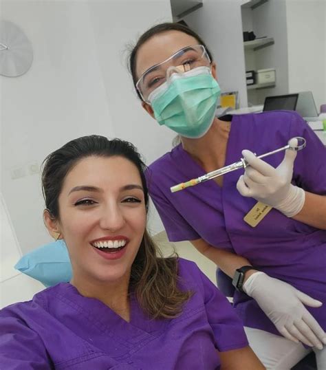 Two Women In Scrubs And Masks Smile At The Camera While Sitting On A Dentist S Chair