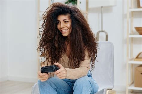 Alegre disfrutó de una bella dama latina rizada y bronceada con joystick gamepad sentarse en una