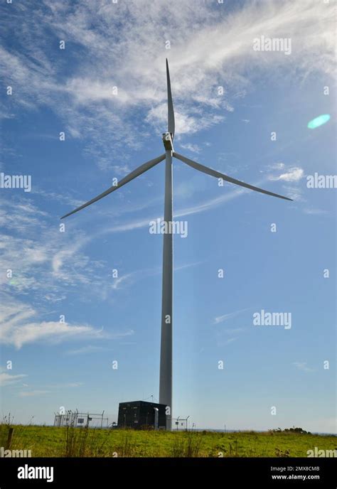 Single Tall Wind Turbine Backlit By The Sun Against A Blue Sky In