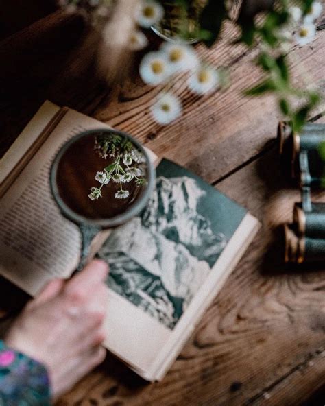 A Person Is Reading A Book And Holding A Cup With Flowers In It On A