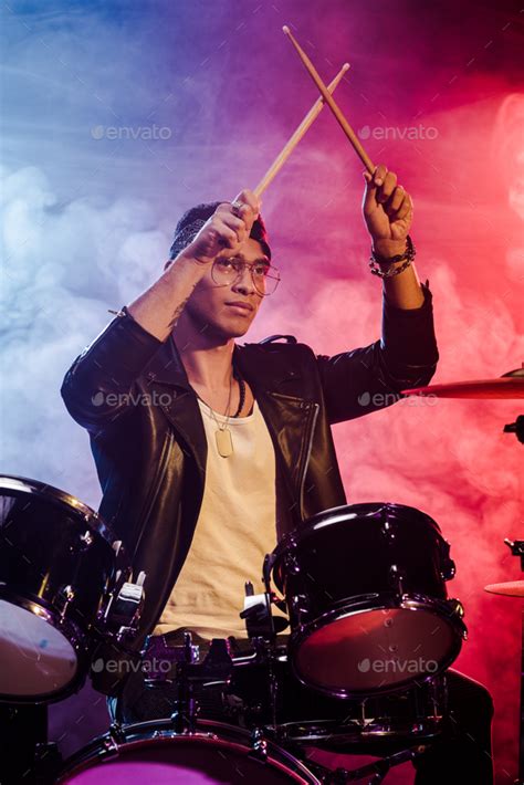 Mixed Race Male Musician Raising Drum Sticks While Sitting Behind Drum