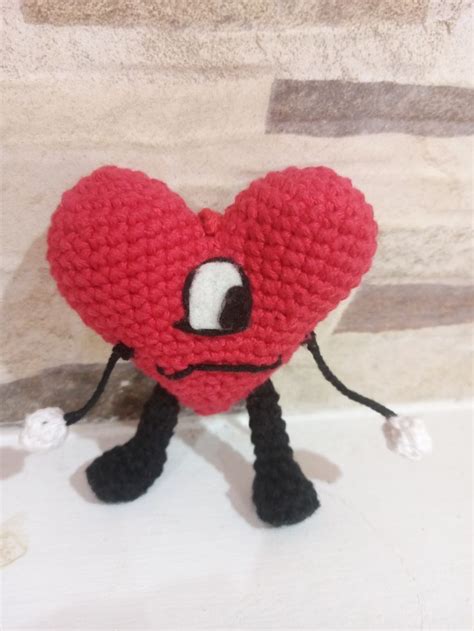 A Red Crocheted Heart With Black Legs And Eyes Sitting On Top Of A