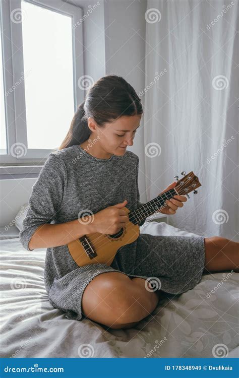 Beautiful Woman Playing Ukulele Sitting At The Bed In Thebedroom