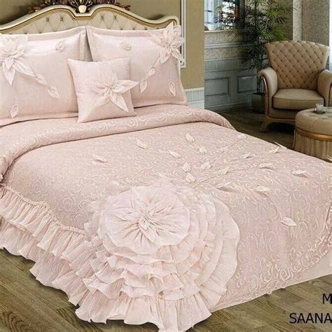 A Bed With Pink Comforter And Pillows On It In A Room Next To A Chair