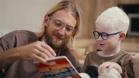 Close-up: a Blond Man with a Beard and Glasses Helps His Little Albino Son with White Hair in ...