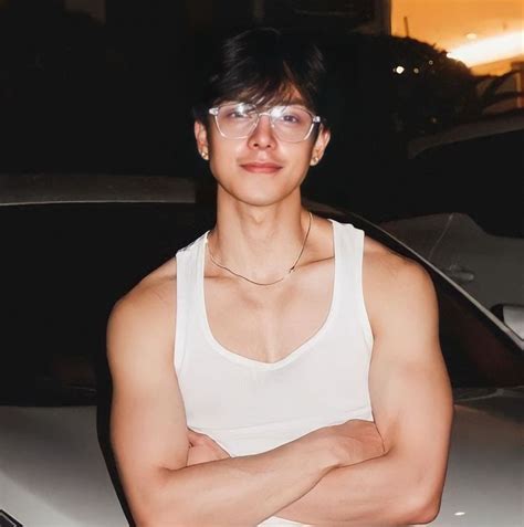 A Man With Glasses Standing In Front Of A Car Wearing A Tank Top And Jeans