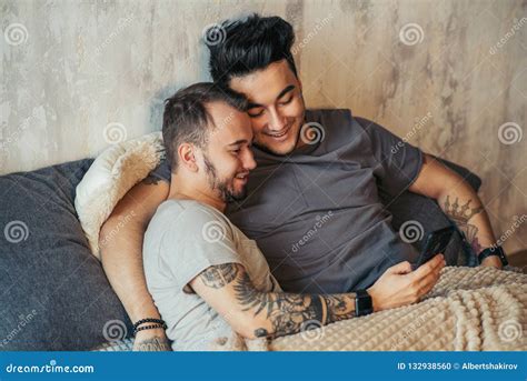 Pares Gay Felices Que Mienten Junto En Cama Y Que Usan El Smartphone Mirando Las Fotos Foto De