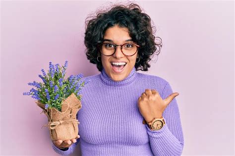 Young Hispanic Woman With Curly Hair Holding Lavender Plant Pointing