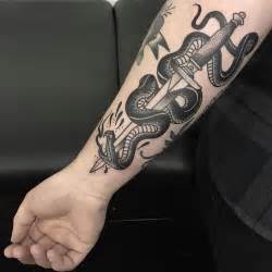 A Man With A Tattoo On His Arm Holding A Knife And Snake Wrapped Around It