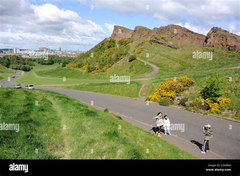 Tourists Take A Picture Next To Salisbury Crags In Holyrood Park In The